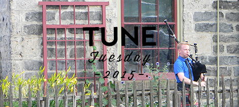 Bagpiper standing in front of stone cottage