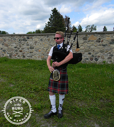 Bagpiper standing outside in front of long stone wall