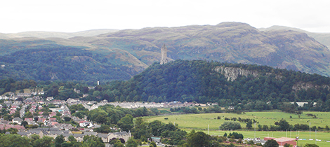 Stone Wallace monument atop green and brown highland hills in Stirling
